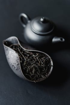 An elegant and sophisticated black teapot is displayed next to a beautifully decorative dish filled with loose leaf tea
