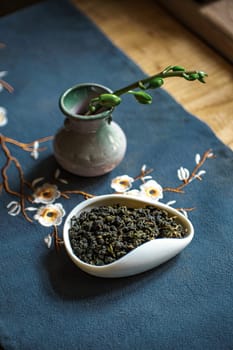 A beautifully arranged setup featuring green tea, an elegant vase, and detailed flowers atop a soft fabric surface