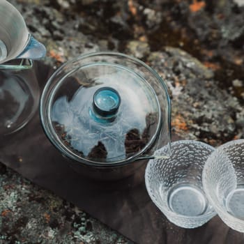 A beautifully styled tea setup showcasing an exquisite glass teapot alongside elegant cups placed atop textured stone