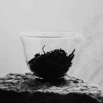 A minimalist black and white photo of tea leaves displayed in a clear cup, highlighting their natural beauty