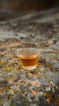 A small glass filled with a beautifully ambercolored beverage is resting gently on a textured rock surface
