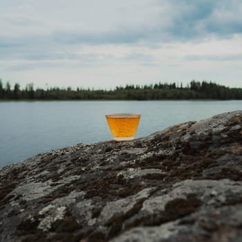A beautifully serene lakeside view showcasing a refreshing drink placed on a rock, capturing natures lovely beauty