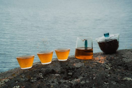 In a serene setting, there are amber beverages placed on a rocky surface beside calm and still waters