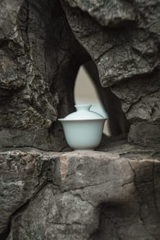 A delicate white teapot is positioned gracefully and elegantly within a rugged rocky formation in nature