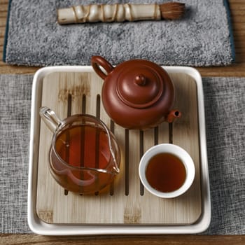 An elegant tea setup showcasing a beautiful clay teapot, a stylish glass pitcher, and a lovely cup on a wooden tray