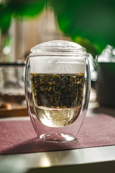 A stunning glass teapot elegantly showcasing a vibrant herbal tea infusion amidst lush greenery behind