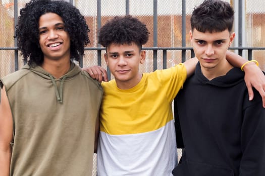 portrait of three multiethnic teen friends hugging looking at camera, concept of friendship and youth lifestyle