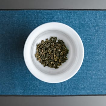 A closeup of dried green tea leaves beautifully arranged in a bowl positioned on vibrant blue fabric background