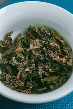 Closeup of dried green tea leaves in a white bowl, showcasing their unique texture and vibrant color