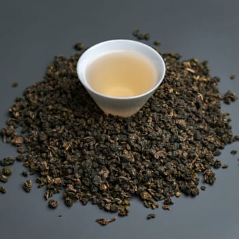 A detailed closeup view of beautifully arranged oolong tea leaves surrounding a warm cup of brewed tea