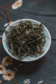 Aesthetic shot of dried green tea leaves on a ceramic plate, set against a floral fabric background