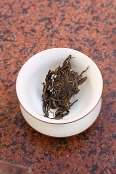 This is a closeup view of dried green tea leaves artistically displayed in a simple white bowl on a textured surface