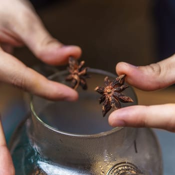 Carefully and thoughtfully adding star anise spice into a glass jar for cooking purposes or decorative uses