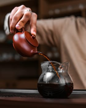 A skilled hand gracefully pours aromatic tea from a timehonored pot into a beautifully designed glass vessel