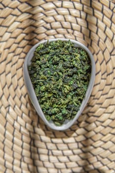 An aesthetic view showcasing dried green herbs beautifully arranged in a ceramic bowl placed on a decorative woven mat