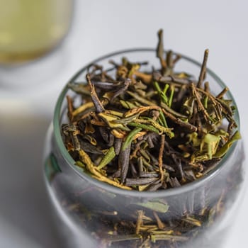 Closeup view of fresh green tea leaves beautifully arranged in a jar, with brewed tea elegantly blurred in background