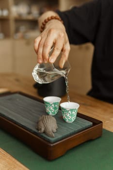 A skilled hand pours aromatic tea into ceramic cups, showcasing craftsmanship in a calm, traditional ceremony