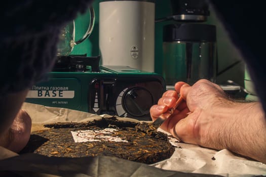 The image shows a closeup of a hand preparing herbal materials with tools on a rustic wooden surface