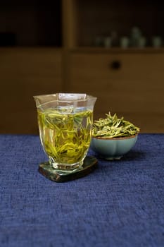 A beautifully arranged glass of vibrant green tea sits elegantly next to fresh herbal leaves on a blue surface