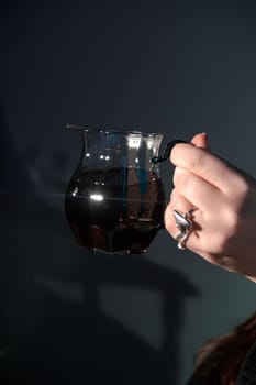 A closeup of a hand holding a glass jug filled with rich liquid, highlighting its elegant design and craftsmanship