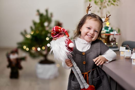 Cute smiling little child girl holding gnome near the Christmas tree at home