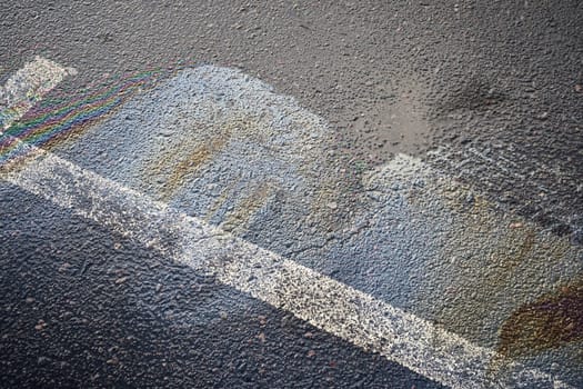 Gasoline or oil spill creating rainbow colors on wet asphalt road surface with white stripe.