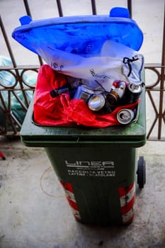 Cremona, Italy - November 7th 2024 Challenges of waste management and recycling showcased in an overflowing green and blue trash bin filled with glass, cans, and bottles