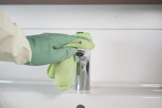 A person diligently cleaning a shiny kitchen faucet using a soft green cloth for optimal results