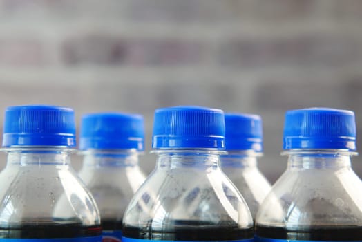 A collection of bottled drinks with blue caps against a textured brick backdrop.