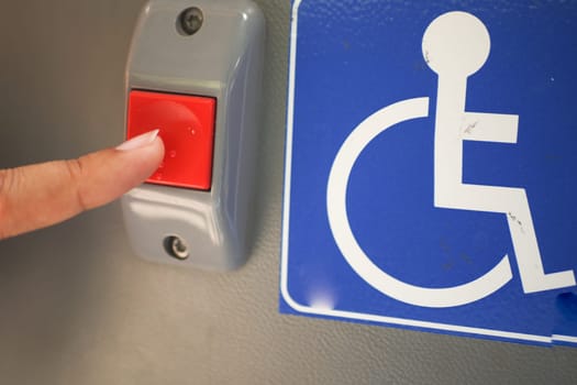 A finger is firmly pressing an accessibility button that is located near a disabled sign