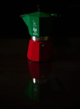 Italian espresso maker in green and red with a striking reflection on a dark surface, capturing a classic kitchen theme.
