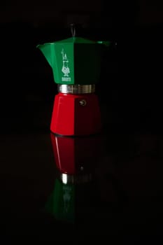 A red and green espresso coffee maker displayed on a reflective surface, enhancing its colorful design.