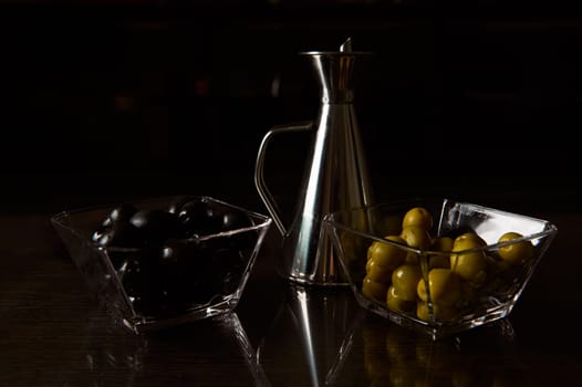 Close-up of dark and moody presentation featuring black and green olives with an olive oil jug. Ideal for culinary themes.