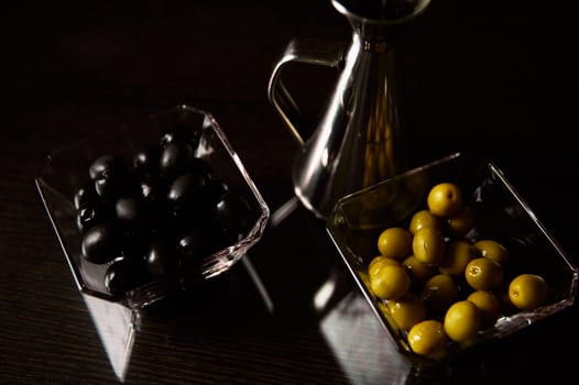 A sophisticated culinary setting featuring black and green olives in glass bowls accompanied by a shiny silver oil jug, highlighting a gourmet kitchen atmosphere.