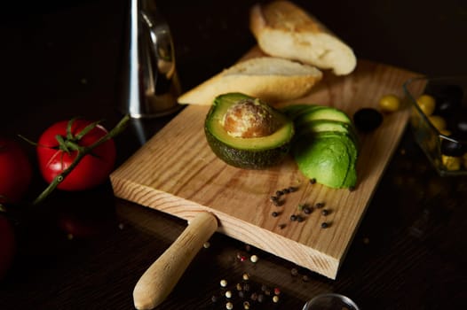 Sliced avocado and crusty bread displayed with vibrant tomatoes and spices on a rustic cutting board, highlighting freshness and simplicity in culinary presentation.