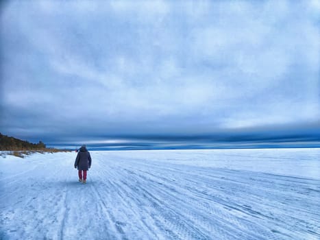 A snowy road along a river in Arkhangelsk shows melting ice, with a person walking on the frozen surface under a cloudy sky.