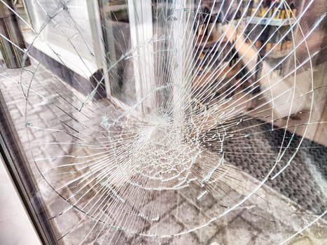 A close-up of shattered glass door window with a spiderweb pattern of cracks