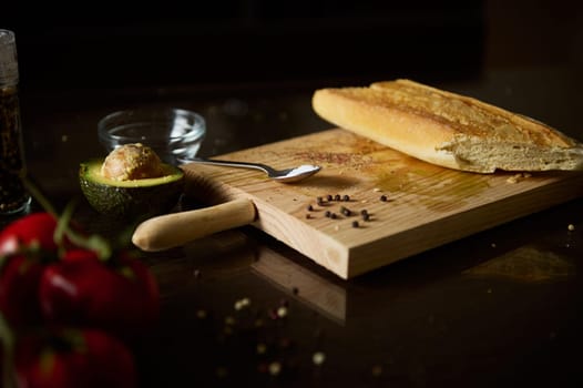 A rustic arrangement featuring fresh bread, avocado, and tomatoes on a dark wooden table. Ideal for organic food, culinary, or rustic kitchen themes.