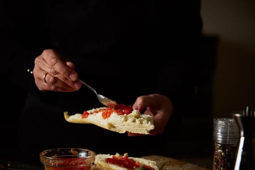 Hands spreading tomato relish on a sandwich bun, ready for a tasty meal.