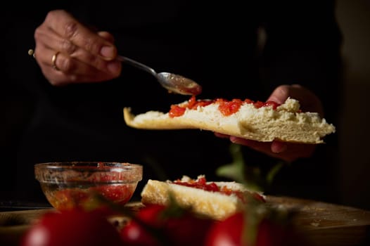 Close-up of hands spreading tomato on bread, creating delicious bruschetta for a meal.