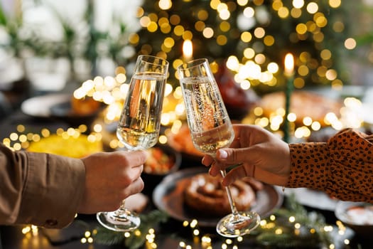 Two people clinking champagne glasses in celebration, with a festive table set for a holiday meal in the background, adorned with lights and decorations.