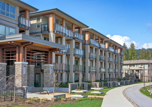 New residential apartment building with walkway and bike route in front on sunny day in British Columbia, Canada.