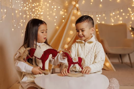Two children playing with toy horses in a cozy room decorated with Christmas lights. children's room