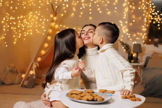 two children kissing mother on christmas evening in cozy room, happy family on christmas,