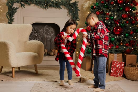 Happy asian children playing with big sweet lollipop candies in cozy room decorated with christmas tree and gilyades, merry christmas