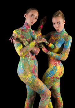 Two nude blondes with colorful bodyart one of them holding a brush isolated cropped shot on black background