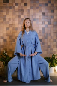 Yoga instructor in blue kimano at fitness gym . The girl does qigong yoga. The exercises are based on the movement of internal energy, the system of channels, energy centers, chakras.