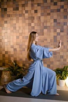 Yoga instructor in blue kimano at fitness gym . The girl does qigong yoga. The exercises are based on the movement of internal energy, the system of channels, energy centers, chakras.