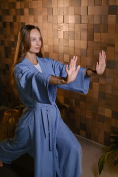Yoga instructor in blue kimano at fitness gym . The girl does qigong yoga. The exercises are based on the movement of internal energy, the system of channels, energy centers, chakras.