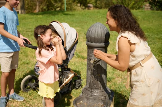 A joyful family with children have fun around a water fountain in a park. A playful moment on a sunny day highlights their closeness and enjoyment of outdoor activities.